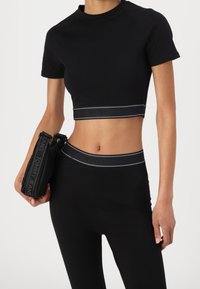 Top noir court et leggings taille haute avec bandes logo. Tissu lisse, manches courtes, coupe près du corps, assortis à un sac pochette noir.