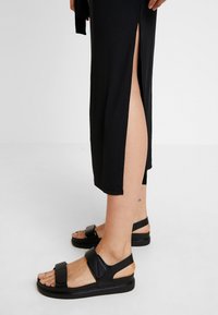 Czarne sandały na platformie z szerokimi paskami, o fakturowanym wykończeniu. Model posiada odkrytą piętę i stabilne paski wokół kostki.