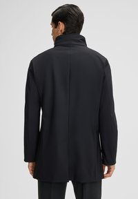 Zwarte lange jas, gemaakt van gladde stof, met een hoge kraag en een rechte snit. De achterkant toont een minimalistisch ontwerp en subtiele naaddetails.