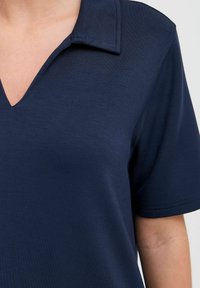 Mörkblå V-ringad t-shirt med korta ärmar, tillverkad av ett mjukt tyg, med en strukturerad krage och subtil textur.