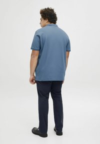 Blauwe polo met korte mouwen in een textuurstof. Gecombineerd met donkerblauwe broeken en zwarte schoenen, bekeken van achteren. Eenvoudig ontwerp.