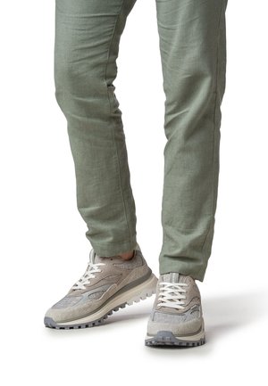 Zapatos deportivos gris claro con tela texturizada y detalles suaves, con cordones blancos y suelas resistentes, combinados con pantalones verdes.