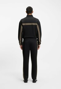 Sort tracksuit med en kravejakke, der har olivengrønne striber. Bukserne er tapered med matchende sidelister og en glat tekstur.