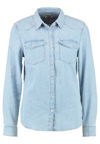 Camicia in denim azzurro chiaro con maniche lunghe, colletto appuntito, due tasche sul petto e chiusura con bottoni. Presenta una leggera texture e dettagli di cucitura.
