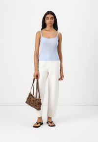 Light blue ribbed tank top with adjustable straps and star embroidery, paired with white wide-leg trousers and a brown textured handbag.