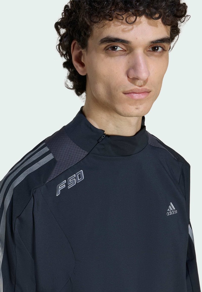 Black athletic jacket featuring a high collar, zip closure, and textured shoulder panels. Includes white accents and “F50” logo on the chest.