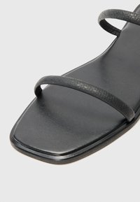 Sorte sandaler med flat såle, med to tynne flettede stroppene, firkantet tådesign og glatt skinntekstur.