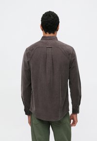 Καφέ πουκάμισο κοτλέ με πτυχώσεις στην πλάτη, μακριά μανίκια, μανσέτες με κουμπιά και στρογγυλεμένη γωνία, συνδυασμένο με παντελόνι λαδί.