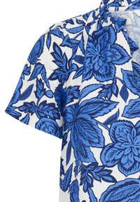 Chemise à manches courtes avec motifs floraux et de feuilles bleus sur fond blanc, dotée d'un col et d'une ouverture partielle à l'avant.