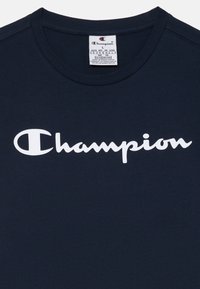 Temno mornarsko modra bombažna majica s poudarjenim belim logotipom "Champion" v kurzivnem slogu, napisanem čez prsni del. Okrogli izrez.