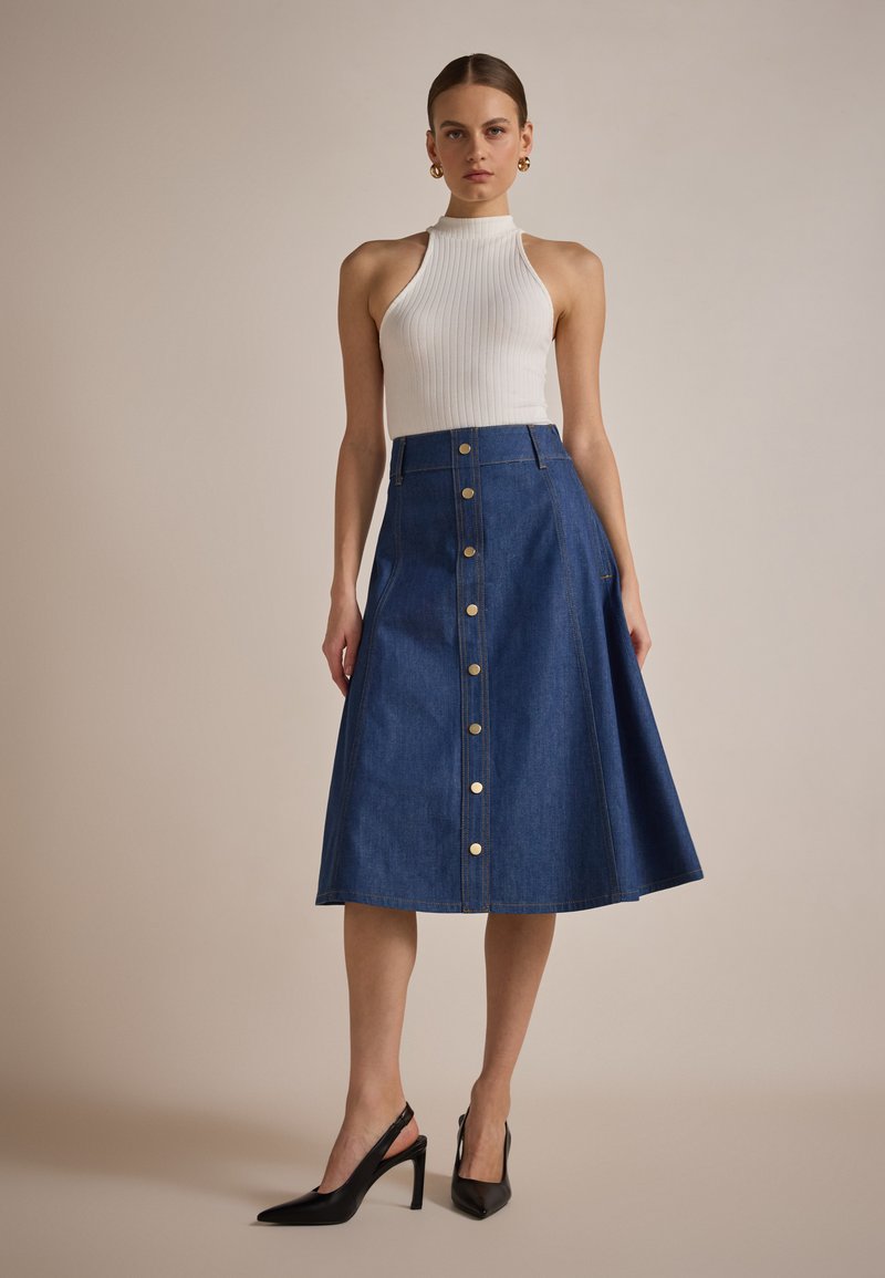 Denim midi skirt with a flared shape, featuring a front button closure and gold-tone buttons, paired with a fitted white ribbed top and black heels.