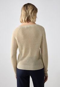 Beige strikkegenser med rund hals og lange ermer. Stoffet har et teksturert, ribbestrikket design og elastisk nederkant og mansjetter.