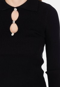 Top lungo a maniche nere a coste con colletto da marinaio e tre scollature a forma di goccia fissate da bottoni decorativi con gemme.