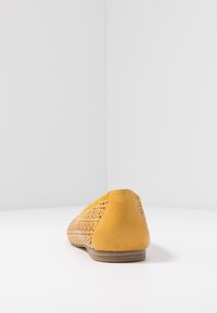 Zapatilla plana de cuero amarilla con diseño recortado, punta redondeada y tacón bajo. Textura suave con una parte trasera sólida para mayor estabilidad.