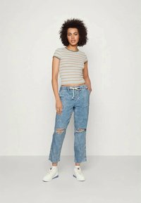 Camisola de manga curta às riscas em bege, verde e branco; jeans claros em azul desgastado com rasgos e cintura elástica; ténis brancos.