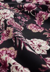 Černá tkanina s květinovým vzorem, která obsahuje bílé, růžové a burgundské květiny a listy v plynulém, zvrásněném textu.