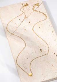 Goldene Halskette mit einem filigranen Design, das einen kleinen herzförmigen Anhänger zeigt. Die Kette hat subtile Glieder und eine strukturierte Oberfläche.
