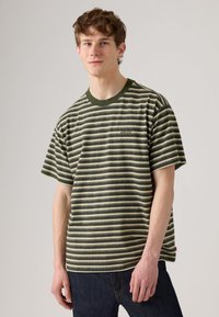 T-shirt com riscas em verde e creme, com riscas horizontais, mangas curtas, gola redonda e um pequeno logotipo no lado esquerdo do peito. Material em algodão.