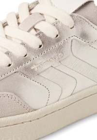 Sneaker mit einem strukturierten, hellgrauen Lederoberteil, cremfarbenen Schnürsenkeln und einer weichen, gemusterten Sohle, die ein dezentes Markenlogo an der Seite trägt.