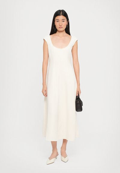 White A-line dress with a scoop neckline and cap sleeves, made from a smooth fabric. Paired with a small black handbag and pointed white shoes.