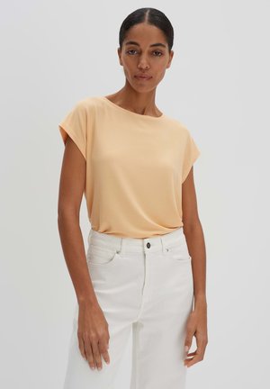 Perzikkleurig T-shirt met korte mouwen, gemaakt van zachte stof, met een losse pasvorm, gecombineerd met witte high-waisted jeans met knoopsluiting.