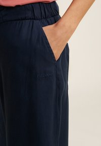 Pantalons navy à taille élastique avec poches latérales, arborant un logo brodé "FREDDY" subtil. Texture lisse, coupe décontractée et matériau léger.
