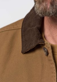 Gros plan d'un homme portant une veste marron avec un col en velours côtelé marron foncé et un bouton visible près du cou.
