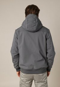Grijze hoodie met een gewatteerde textuur op de capuchon, met een rits aan de voorkant en geribbelde manchetten en zoom, gezien van achteren.