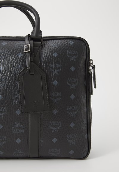 Black textured leather laptop bag with embossed diamond pattern and logo. Features a top handle, detachable tag, and zip closure.