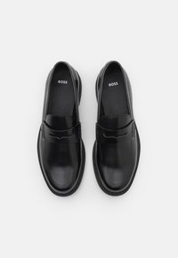 Melnas ādas loafers ar gludu apdari, ar šuvi izšūtu akcentu augšpusē un subtīlu logotipu uz iekšzoles. Apaļa pirksta forma.