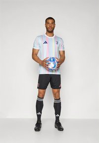 Juventus-Fußballtrikot mit einem pastellgestreiften Trikot in Blau, Pink und Weiß, schwarzen Shorts, schwarzen Socken mit weißen Streifen und schwarzen Fußballschuhen.