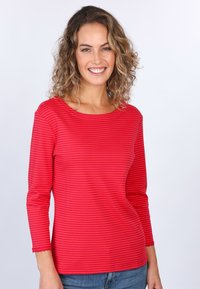 Langärmliges Oberteil mit roten Streifen, rundem Ausschnitt und gewelltem Saum, aus weichem Stoff. Kombiniert mit blauen Jeans.