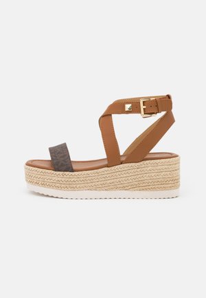 Braune Zehentrenner-Sandalen mit einer geflochtenen Jutesohle, ausgestattet mit einem oberen Riemen aus dunklem Textil und einem Kreuzriemen-Design mit einem goldfarbenen Schnallenakzent.