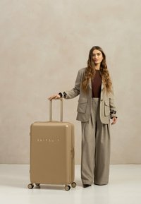 Beige Hartschalenkoffer mit glänzender Oberfläche, ausgestattet mit einem ausziehbaren Griff, vier Rollen und dem eingeprägten Markennamen "SUITSUIT."