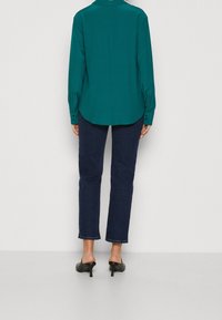 Blusa verde acqua con colletto, maniche lunghe e polsini con bottoni, abbinata a jeans dritti blu scuro e mule neri con tacco.