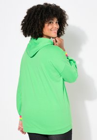 Felpa verde realizzata in un tessuto morbido, con tasca a marsupio e accenti a righe colorate sulle maniche. Vestibilità comoda con cappuccio.