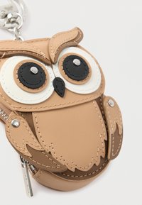 Cartera llavero con forma de búho hecha de cuero beige. Presenta grandes ojos negros y blancos, detalles cosidos y un tirador de cremallera plateado.
