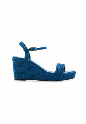 Sandalias de cuña azules fabricadas en material trenzado. Cuentan con una sola correa en la parte de los dedos y una correa ajustable en el tobillo. Diseño de superficie texturizada.