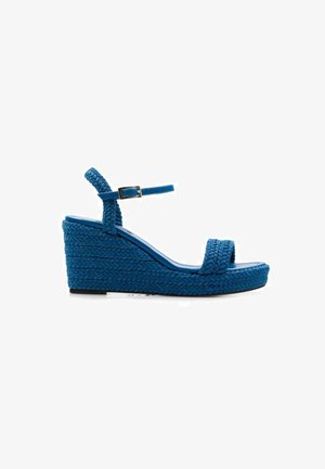 Sandalias de cuña azules fabricadas en material trenzado. Cuentan con una sola correa en la parte de los dedos y una correa ajustable en el tobillo. Diseño de superficie texturizada.