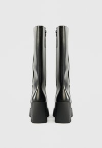 Melnas ceļgalu auguma zābakus ar gludas patentētas ādas apdari, masīviem blokveida papēžiem un sānu rāvējslēdzējiem, ar noapaļotu purngalu dizainu.