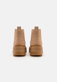 Svijetlosmeđi nubuk čizmi s visokom dizajnom, koje imaju robusnu gumenu potplat i stražnju ručku za povlačenje. Timberland logo utisnut na peti.