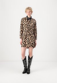 Leopardu raksta kleita ar jostu viduklī, garām piedurknēm un apkakli. Kombinēta ar garām melnām kovboju zābakiem, kuriem ir balta izšuvuma detaļas.