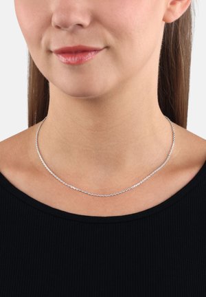 Collana choker argento con un design a catena delicato, caratterizzata da piccoli anelli rotondi. Indossata intorno al collo sopra un top nero. Texture liscia.