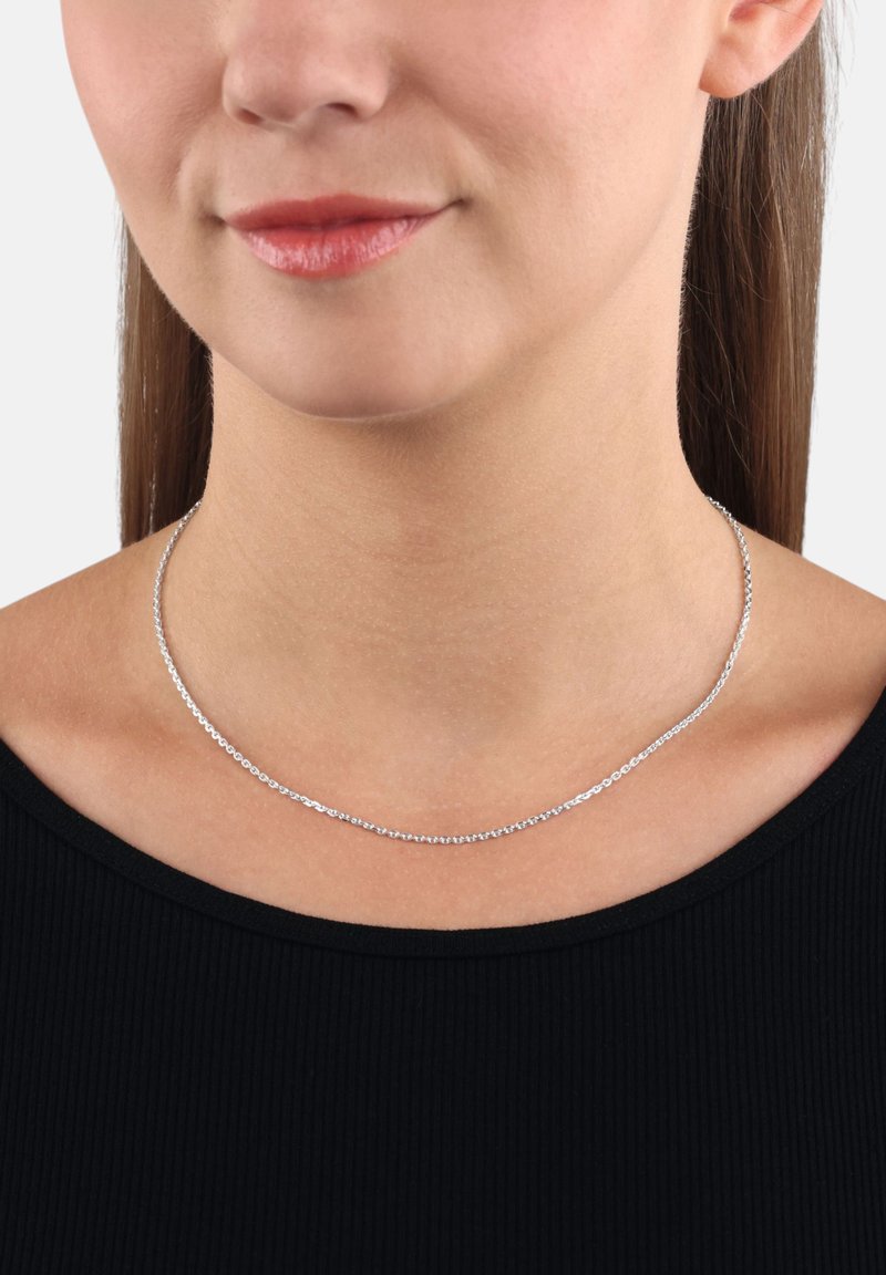 Collana choker argento con un design a catena delicato, caratterizzata da piccoli anelli rotondi. Indossata intorno al collo sopra un top nero. Texture liscia.