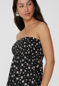 Schwarzes trägerloses Kleid mit Blumenmuster, das kleine rosa Blüten und grüne Blätter zeigt. Leichter Stoff mit einem gerafften Oberteil.
