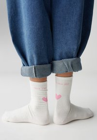 Calze bianche a coste con motivi di cuori rosa e il testo "have a nice day." Indossate con pantaloni di denim blu arrotolati.