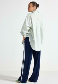 Ljusgrön och vit randig oversized skjorta med uppvikta ärmar; matchad med marinblå vida byxor med vita sidosträck.