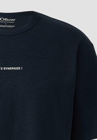 T-shirt bleu marine foncé à col rond avec texte blanc partiel "SYNERGIZE!" sur le devant et étiquette de la marque "s.Oliver" à l'intérieur du col.