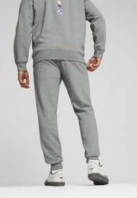 Sive hlače in ujemajoča majica iz mehkega materiala. Obleka ima rebraste manšete in oznako logotipa na hrbtni strani. Vključeni so beli tenis škornji.
