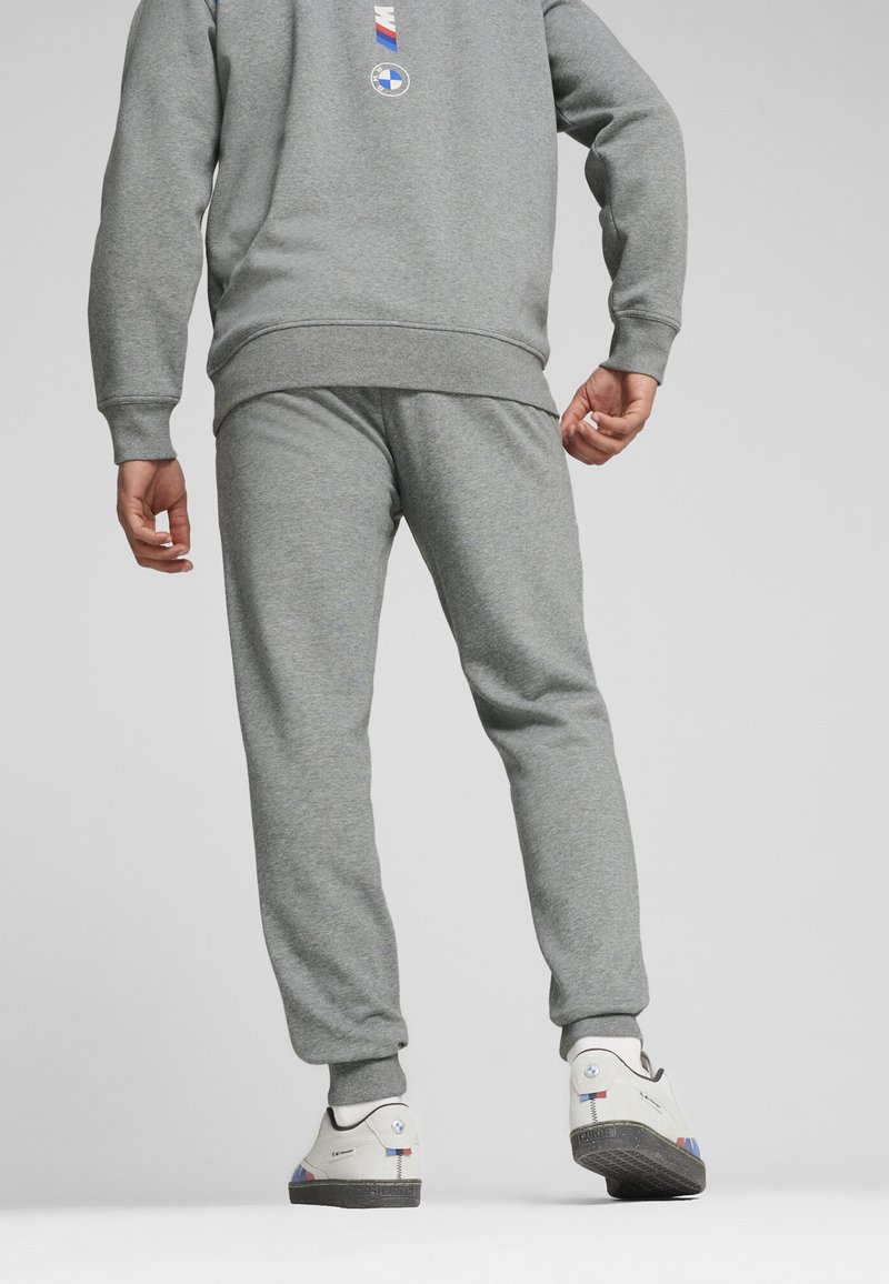 Sive hlače in ujemajoča majica iz mehkega materiala. Obleka ima rebraste manšete in oznako logotipa na hrbtni strani. Vključeni so beli tenis škornji.